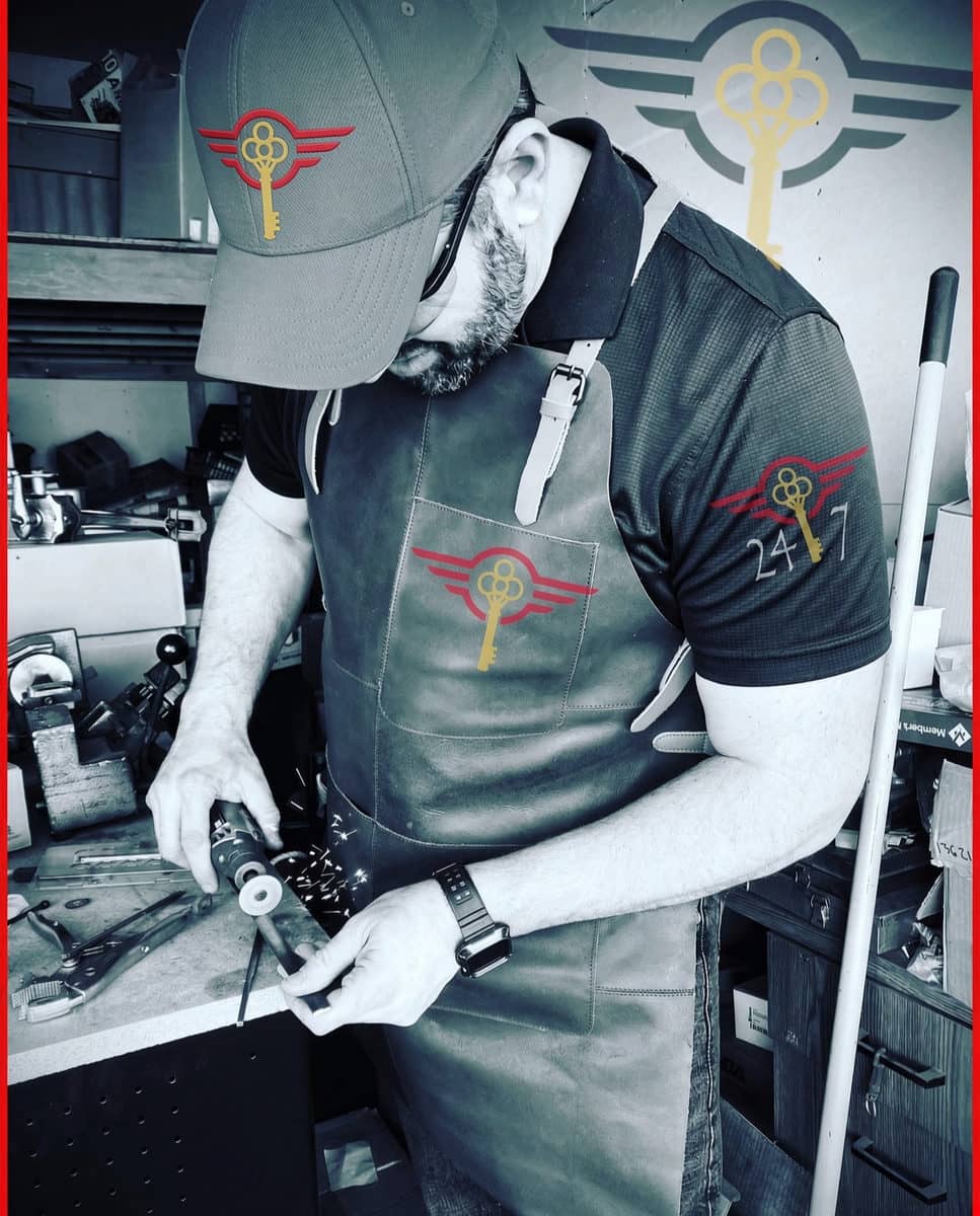 Adam, third-generation master locksmith, at the bench in a Legacy Locksmiths cap and apron