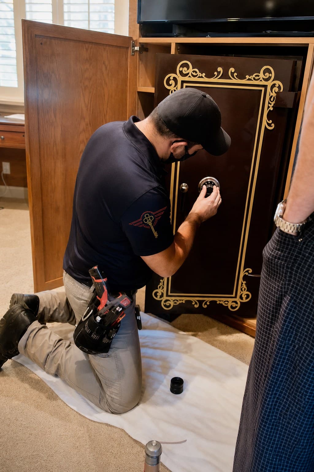 Locksmith kneeling on a drop cloth, servicing a residential safe combination dial